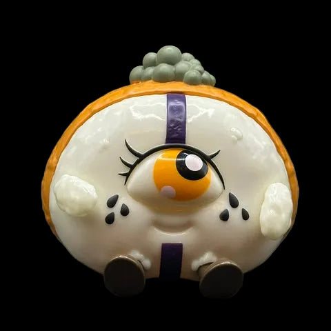 A cute, round character figurine resembling a stylized fried egg or dumpling with a single large eye, black eyelashes, small black spots, a purple vertical stripe, and gray-green tufts on top, set against a dark gray background.

Made by Monster Mind